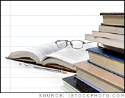 Open book with glasses and pen behind a stack of books